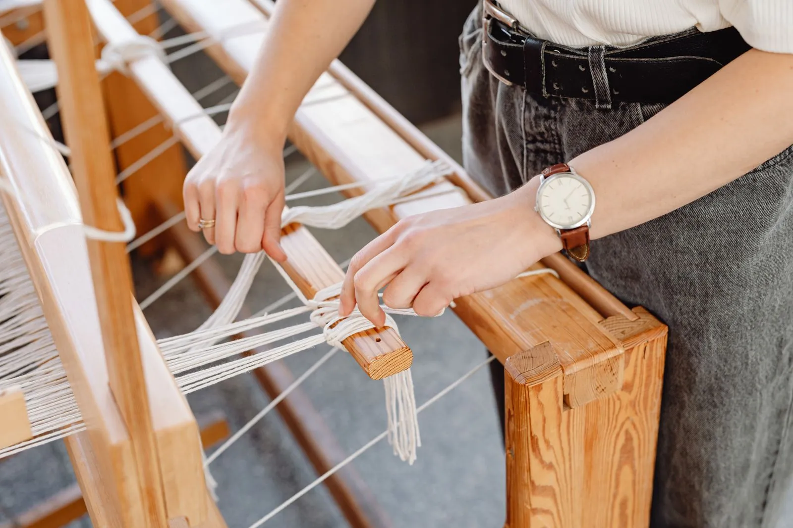 Hands of a woman weaving fabric on a wooden loom, capturing the art of craftsmanship.