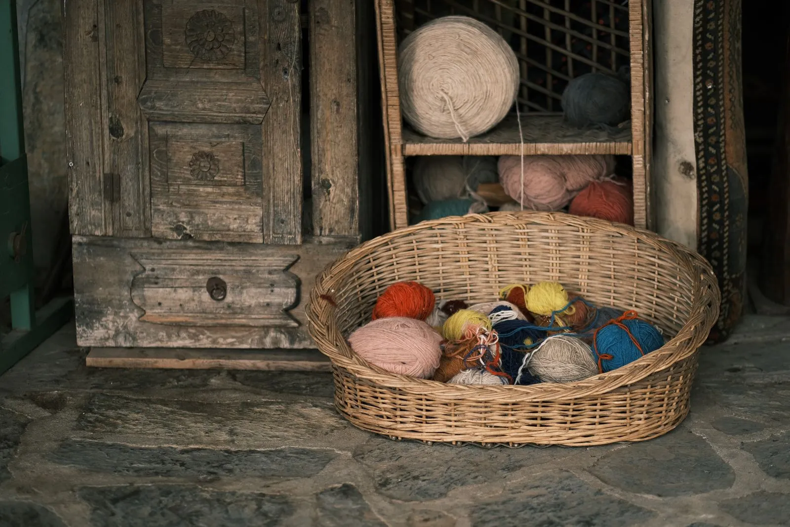 Colorful yarn balls in a wicker basket beside a rustic wooden cabinet, perfect for crafting inspiration.